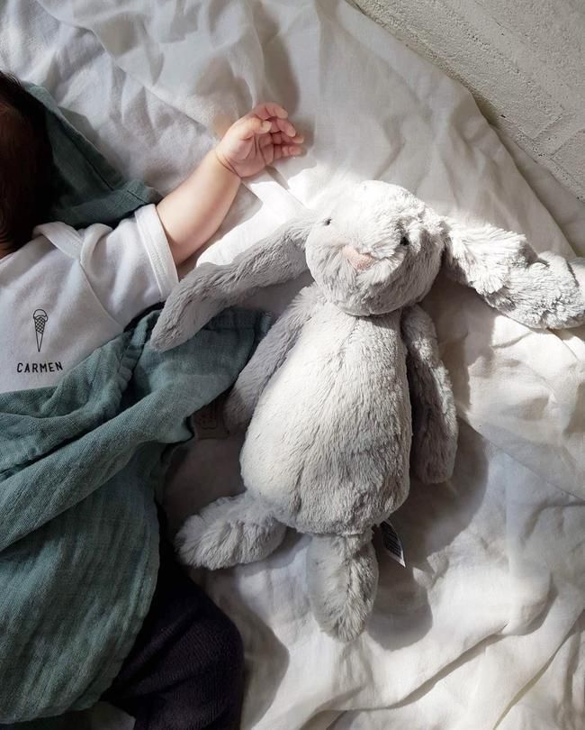 a baby laying in bed next to a stuffed bunny rabbit toy and blanket on top of it's back