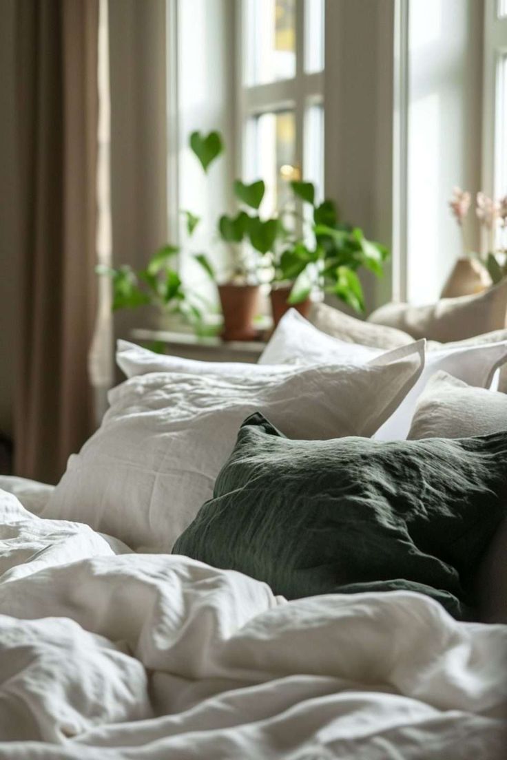 a bed with white linens and pillows in front of two large potted plants