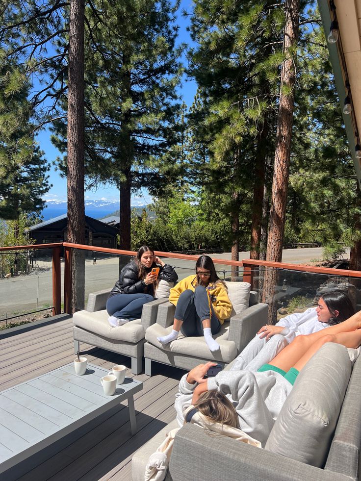 three people sitting on couches on a deck with pine trees in the back ground