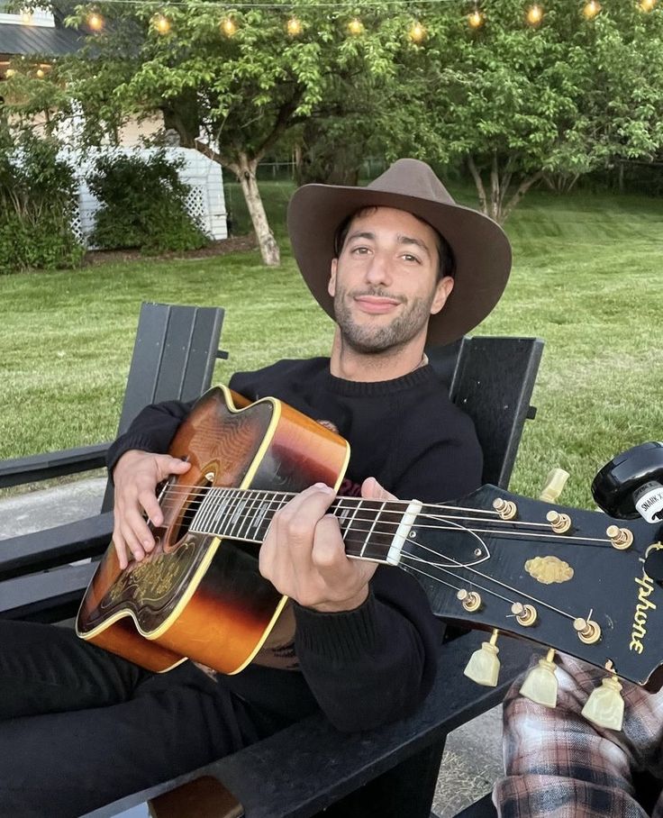 a man sitting on a bench holding an acoustic guitar and wearing a cowboy hat while playing the guitar