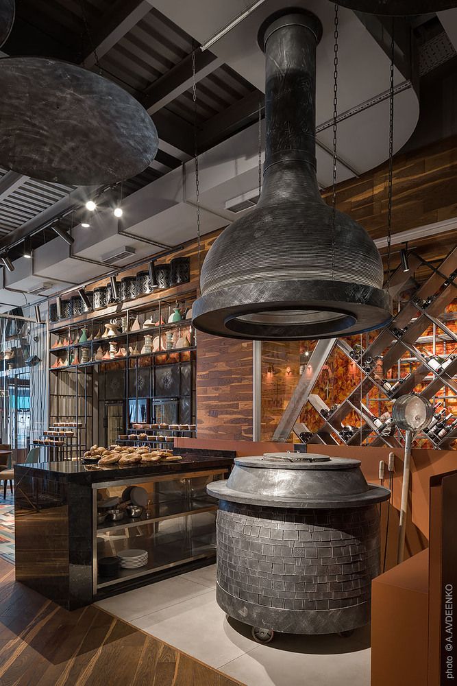 an industrial style kitchen and dining area in a restaurant with wood floors, exposed lighting, and hanging pendants