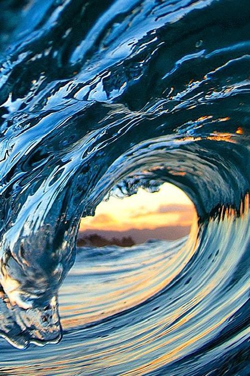 an ocean wave is shown with the sun setting in the background and water splashing on it