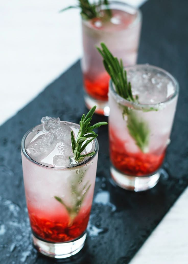 three glasses filled with ice and garnish on top of a black countertop