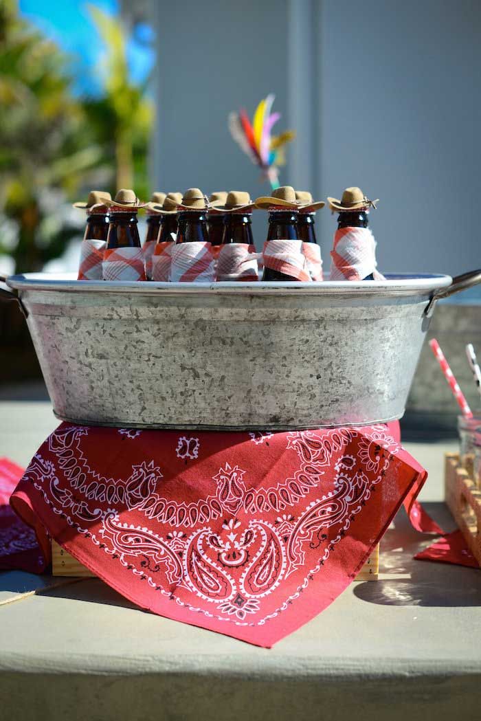 several bottles of beer are sitting in an ice bucket with red bandannas on the table