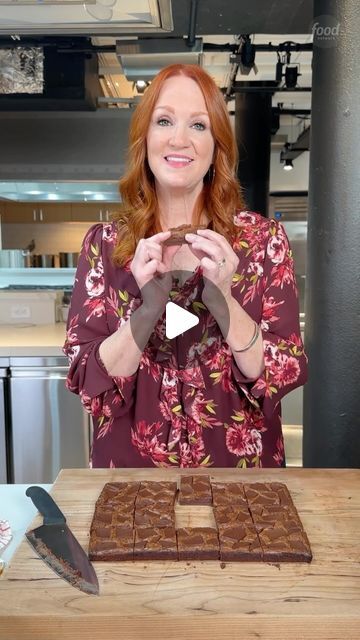 a woman standing in front of a cutting board with chocolate squares on it