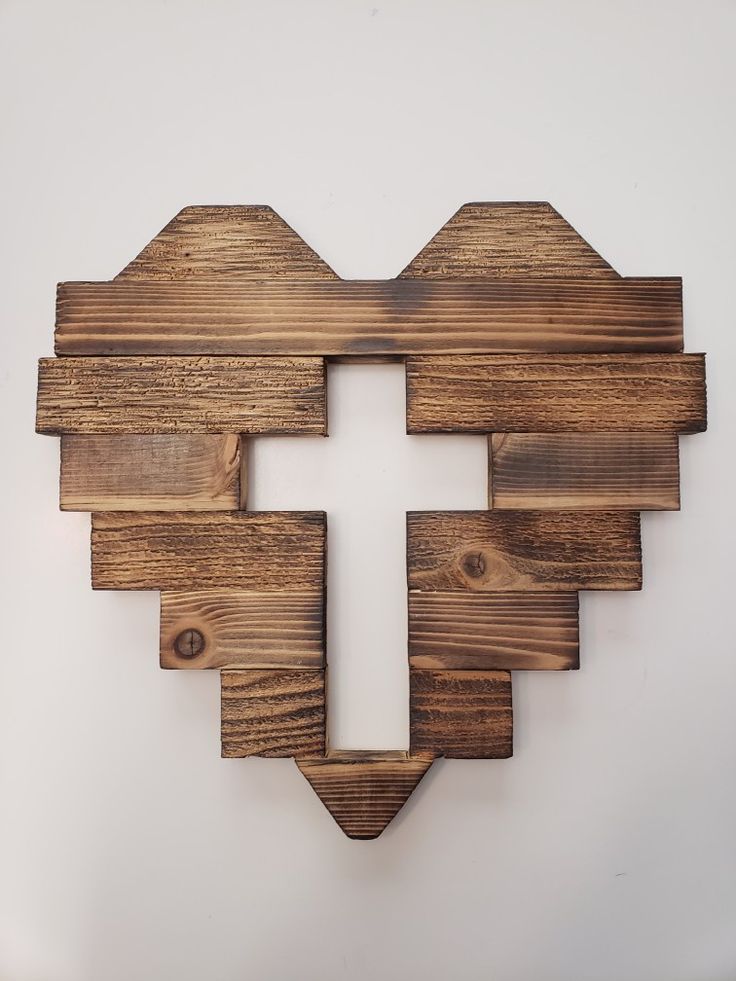 a cross made out of wooden planks on a white wall in the shape of a heart