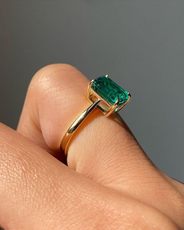 a close up of a person's hand holding a ring with an emerald stone