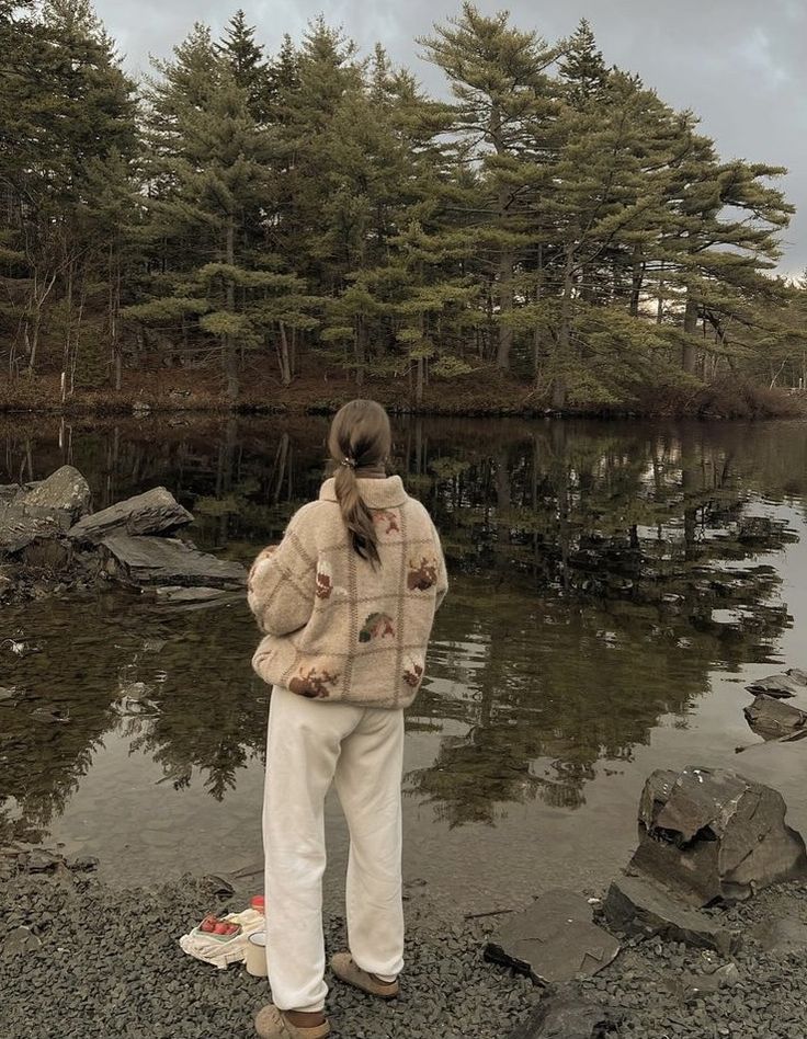 a woman standing in front of a body of water with trees behind her and trash on the ground