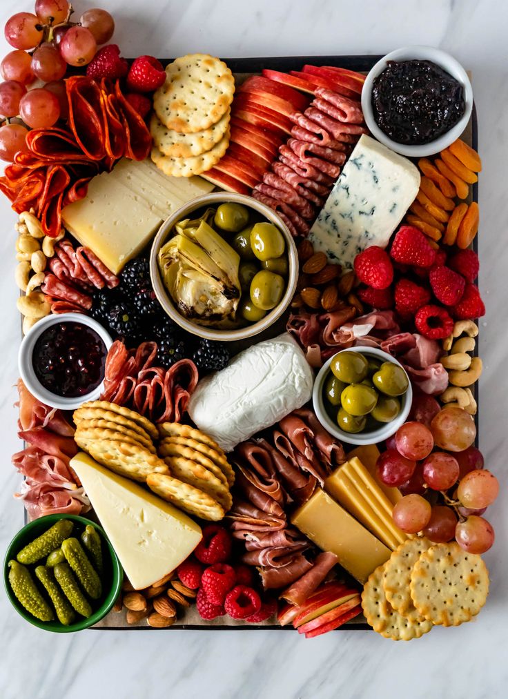 an assortment of cheeses, crackers, fruits and nuts on a platter