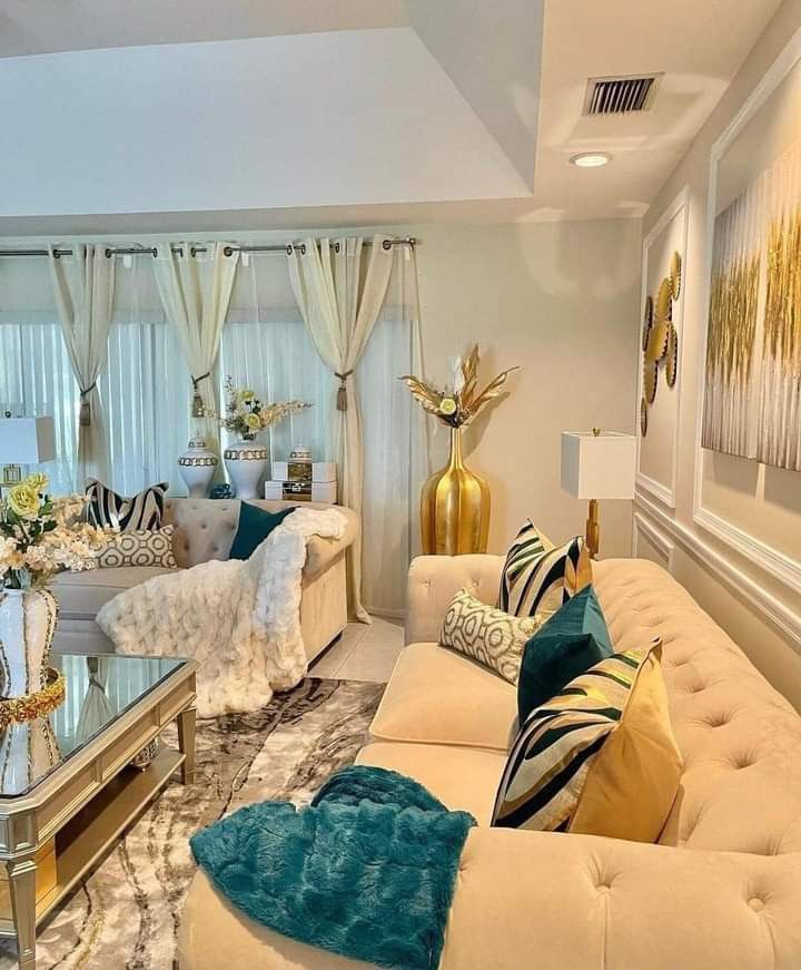 a living room filled with lots of white furniture and gold accessories on top of it