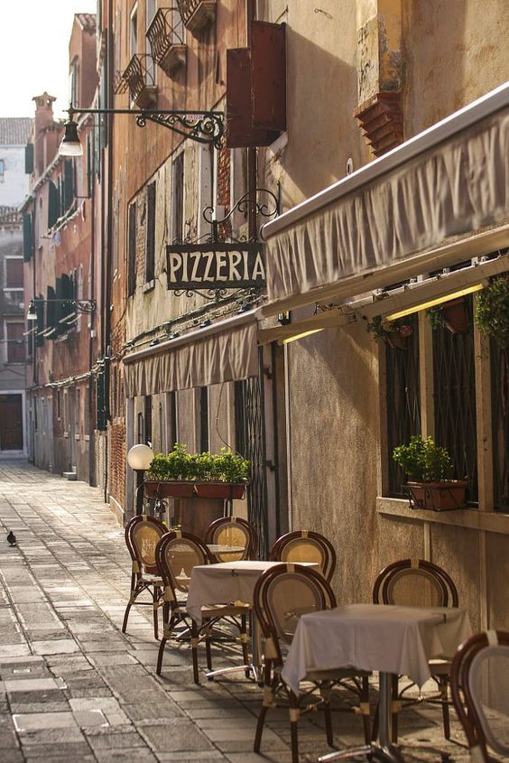 an empty street with tables and chairs in front of the building that houses pizzeria