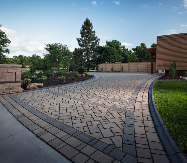 a brick driveway surrounded by green grass and trees