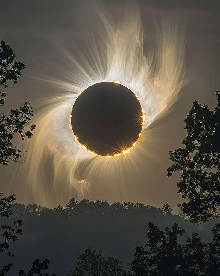 the sun is partially obscured by clouds as it moves through the sky in front of trees