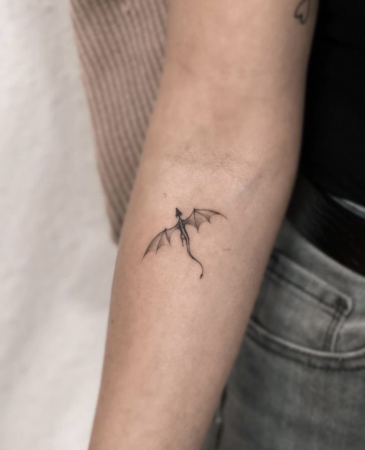 a woman's arm with a small dragon tattoo on the left side of her arm