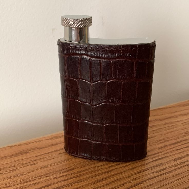 a flask shaped like a crocodile skin leather with a silver top on a wooden table