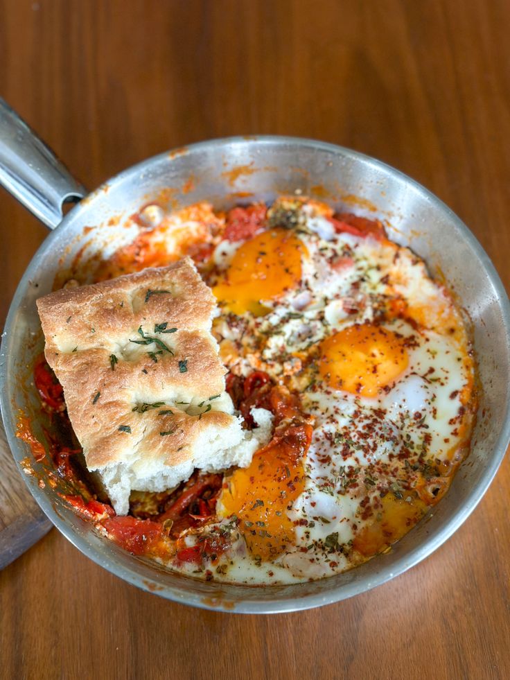 an omelet with eggs, tomatoes and herbs in a pan on a wooden table