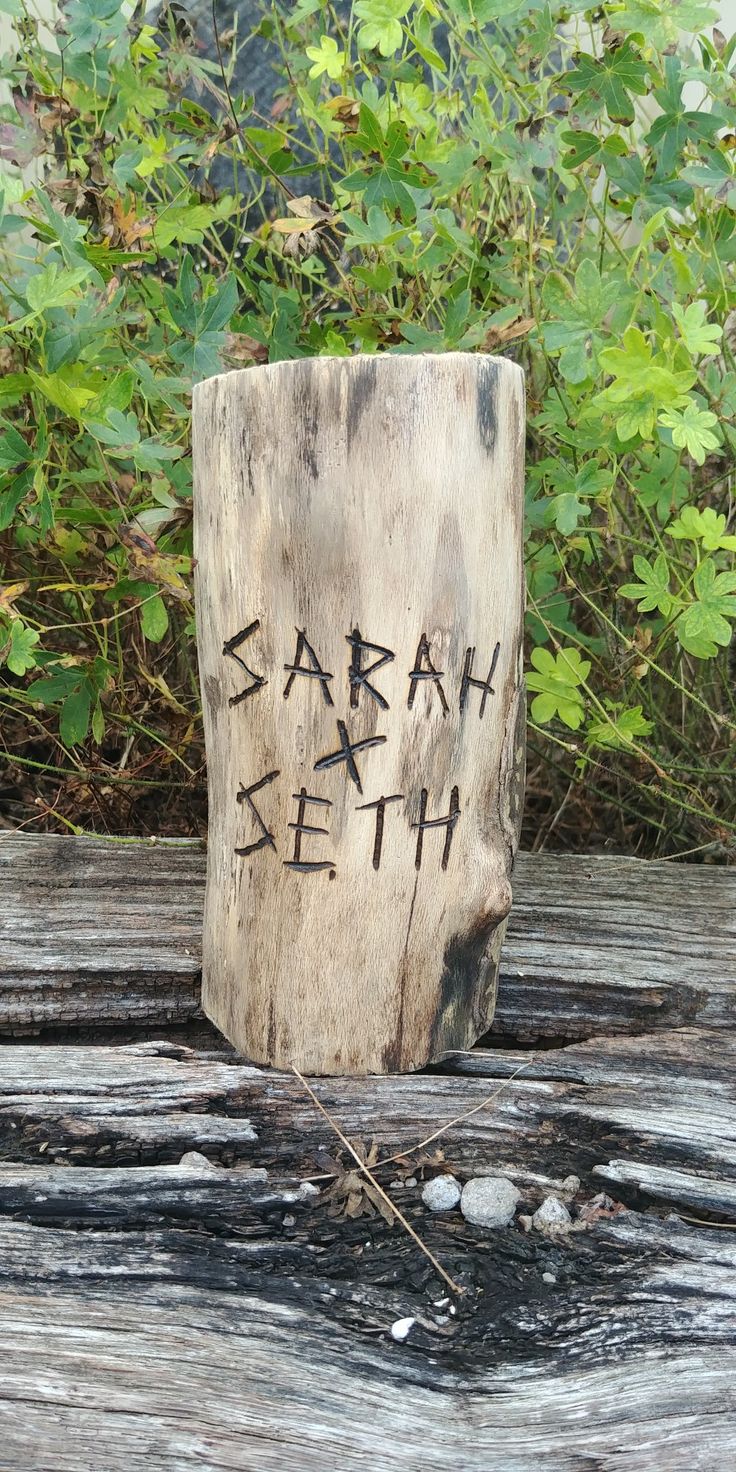 a piece of wood with writing on it sitting on top of a wooden table next to some plants