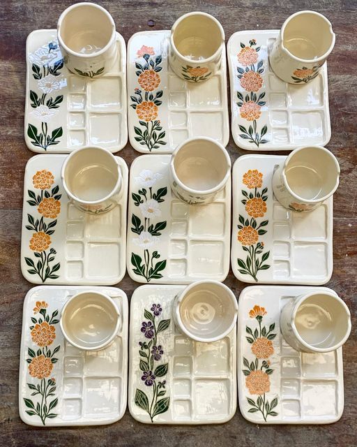 six white dishes with flowers painted on them and cups in the middle one is filled with water