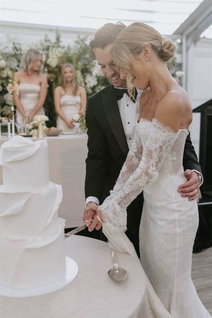 a bride and groom cutting their wedding cake together at the reception table with other people in the background