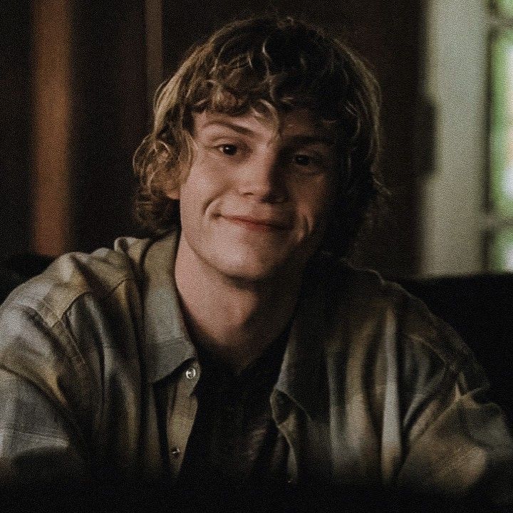 a smiling young man sitting in front of a window