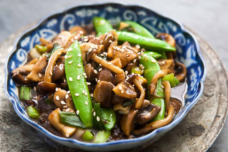 a blue and white bowl filled with stir fry mushrooms, asparagus and sesame seeds