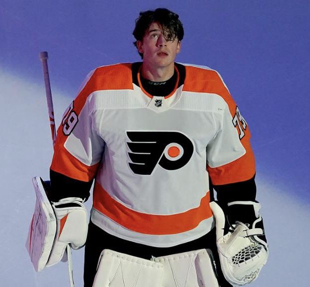 a man in an orange and white jersey holding a hockey stick