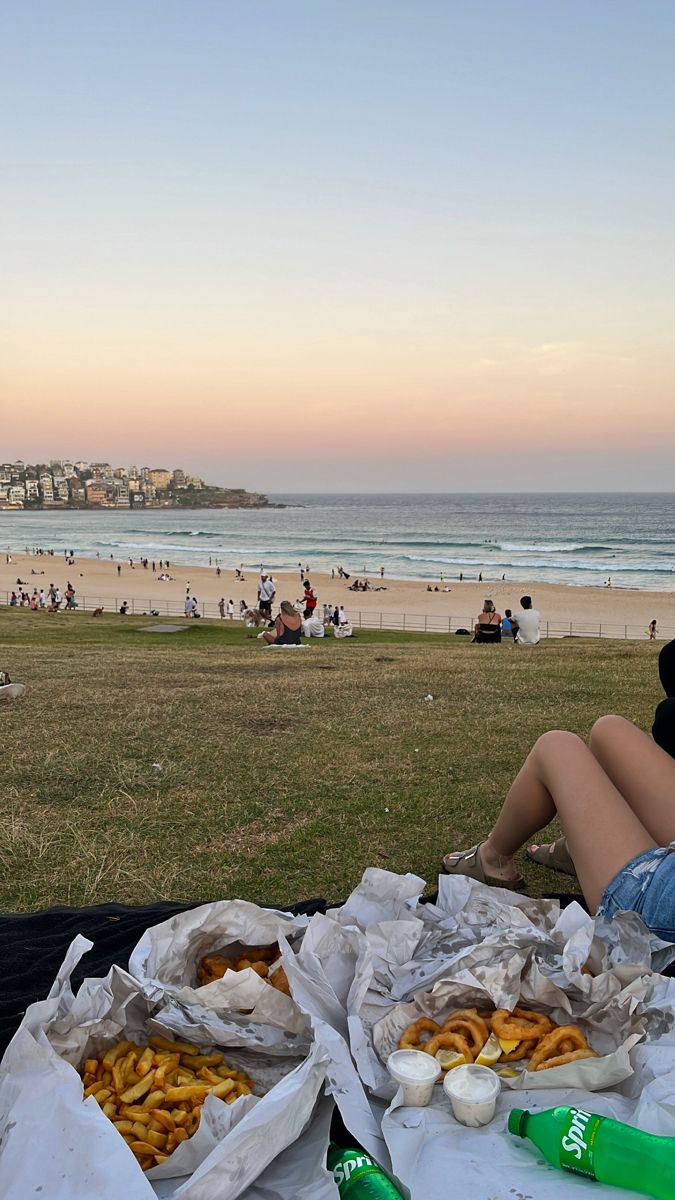 a woman sitting on the beach with two bags of food