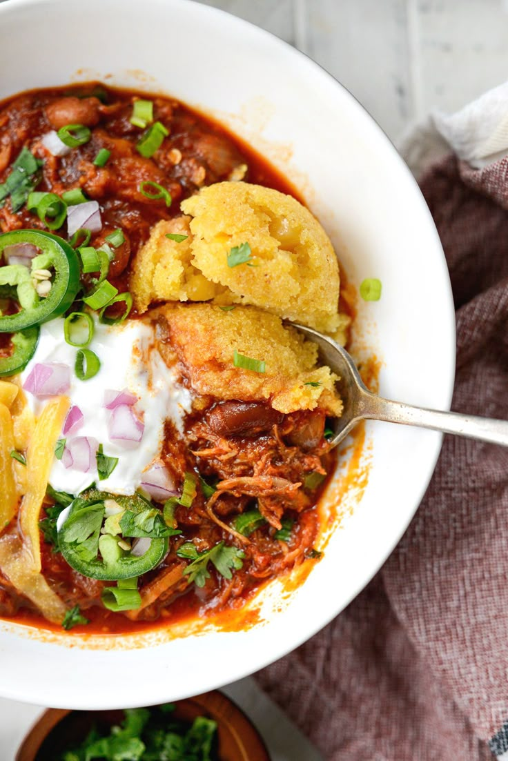 a white bowl filled with chili, meat and tortilla bread topped with sour cream