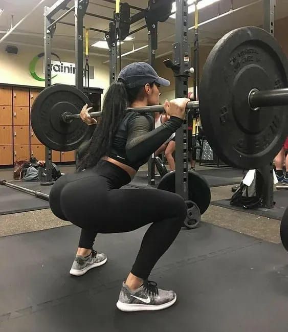 a woman doing squats with a barbell in a gym