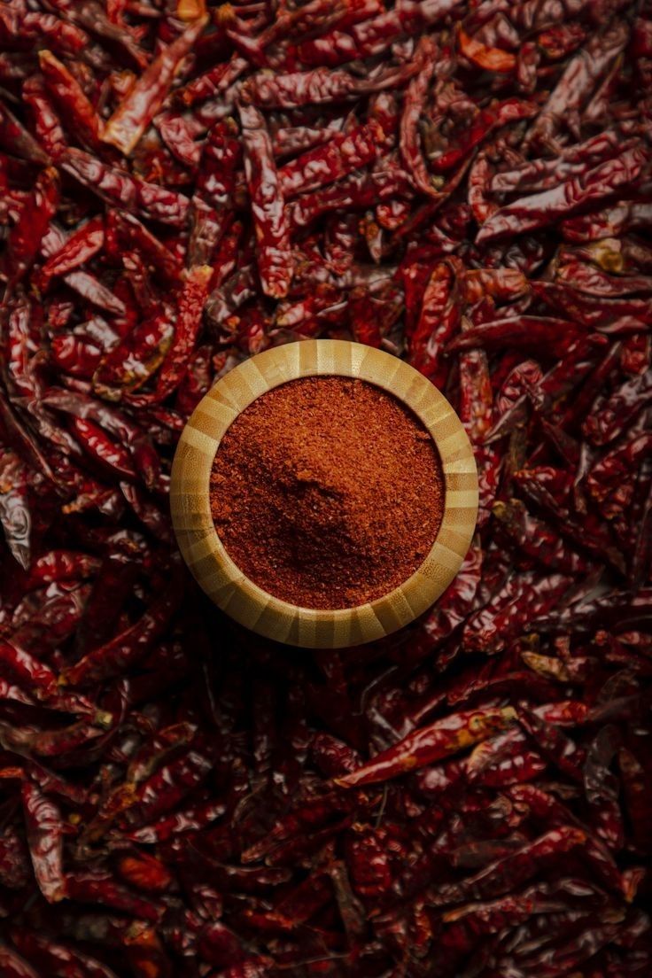 a wooden bowl filled with red chilli on top of a pile of chili peppers