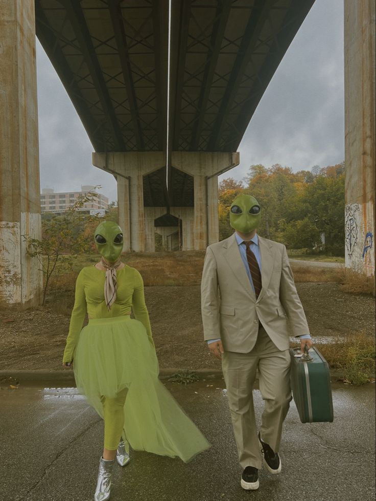 two people in alien costumes walking under a bridge