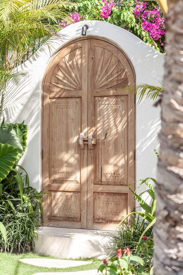 an arched wooden door in front of a white wall with pink flowers and palm trees