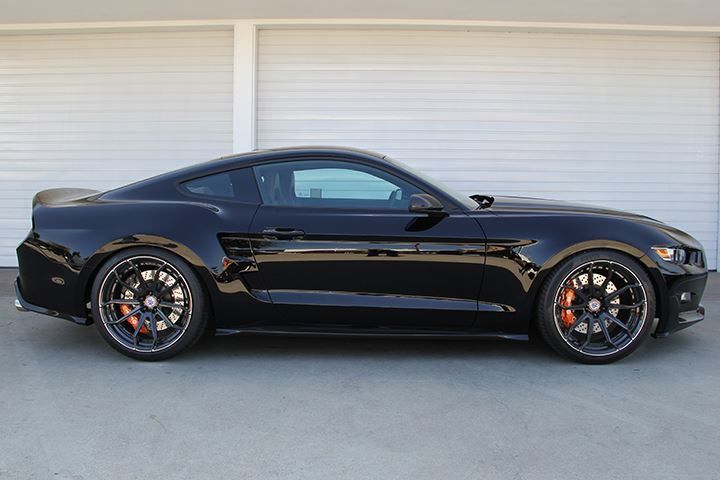 a black sports car parked in front of a garage with two white garage doors behind it