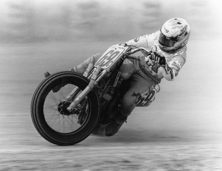 a man riding on the back of a motorcycle down a hill in black and white