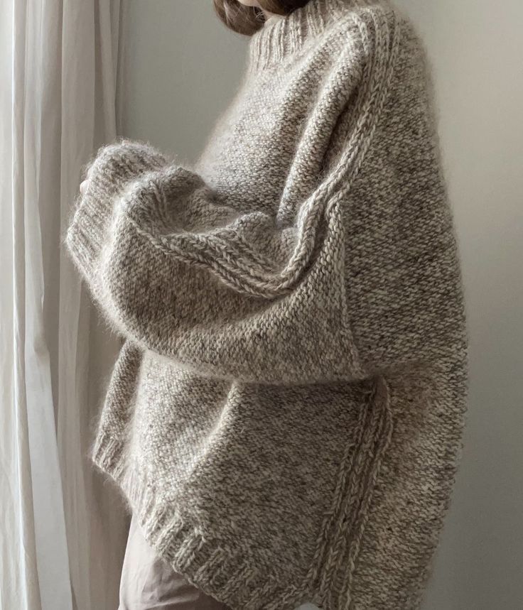 a woman standing in front of a window wearing a sweater