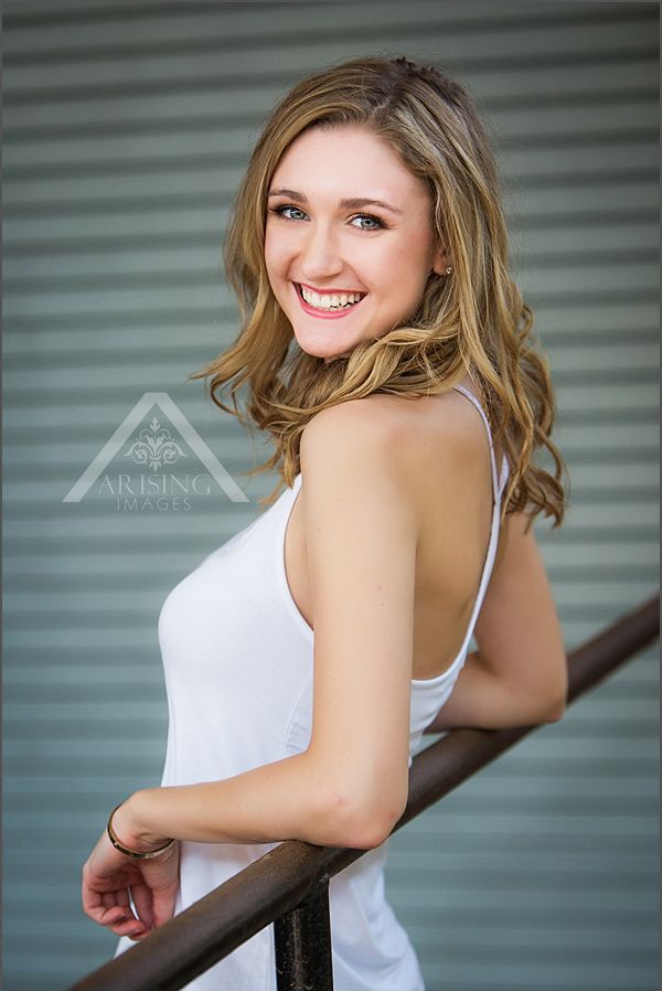 a beautiful young woman standing on top of a metal rail smiling at the camera with her hand on her hips