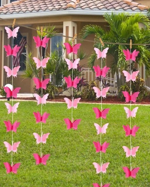 some pink butterflies are in the grass near a house and trees with flags on them