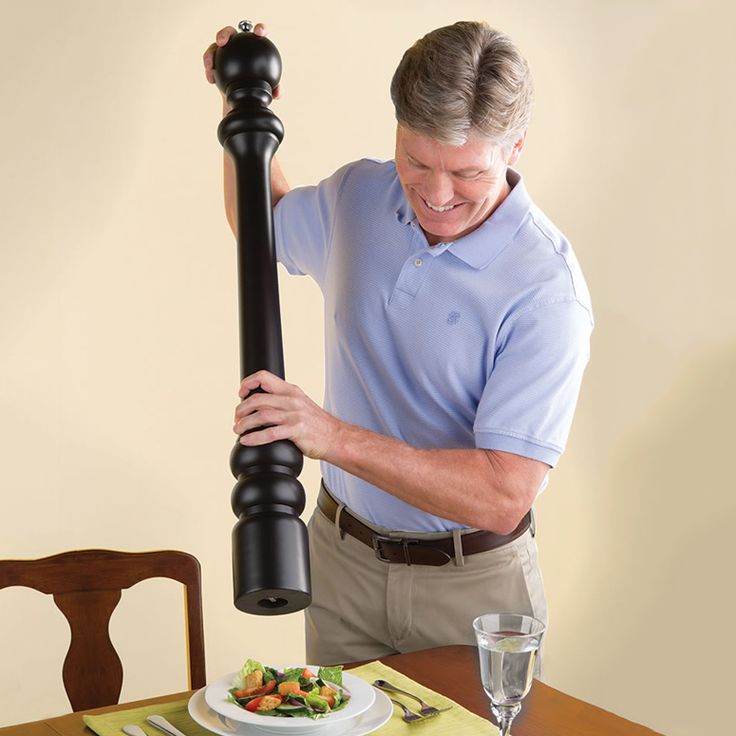 a man holding a large black object on top of a wooden table next to a plate of food