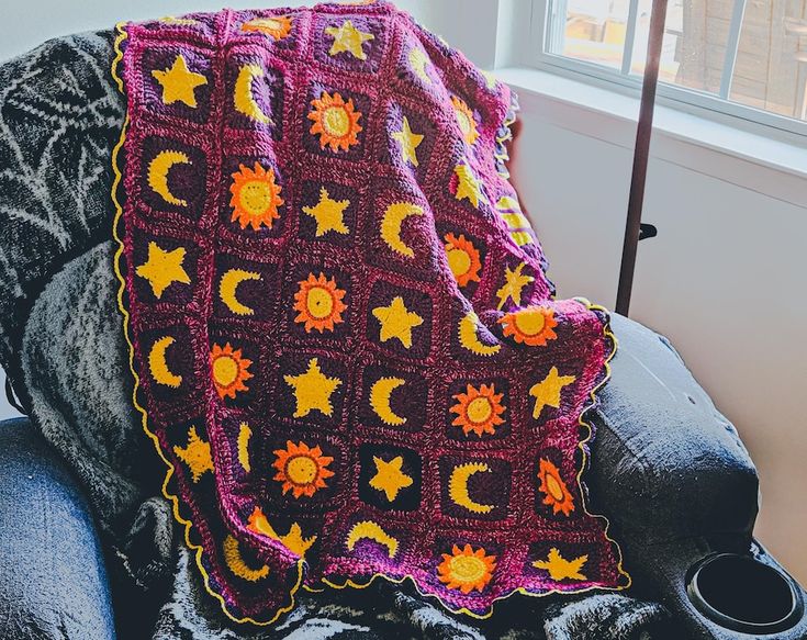 a crocheted blanket sitting on top of a couch next to a cup and window