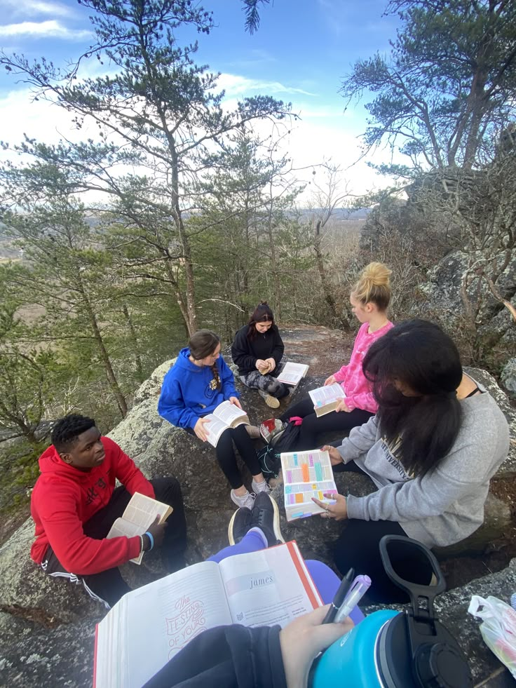 four people are sitting on the edge of a cliff and looking at papers in their hands