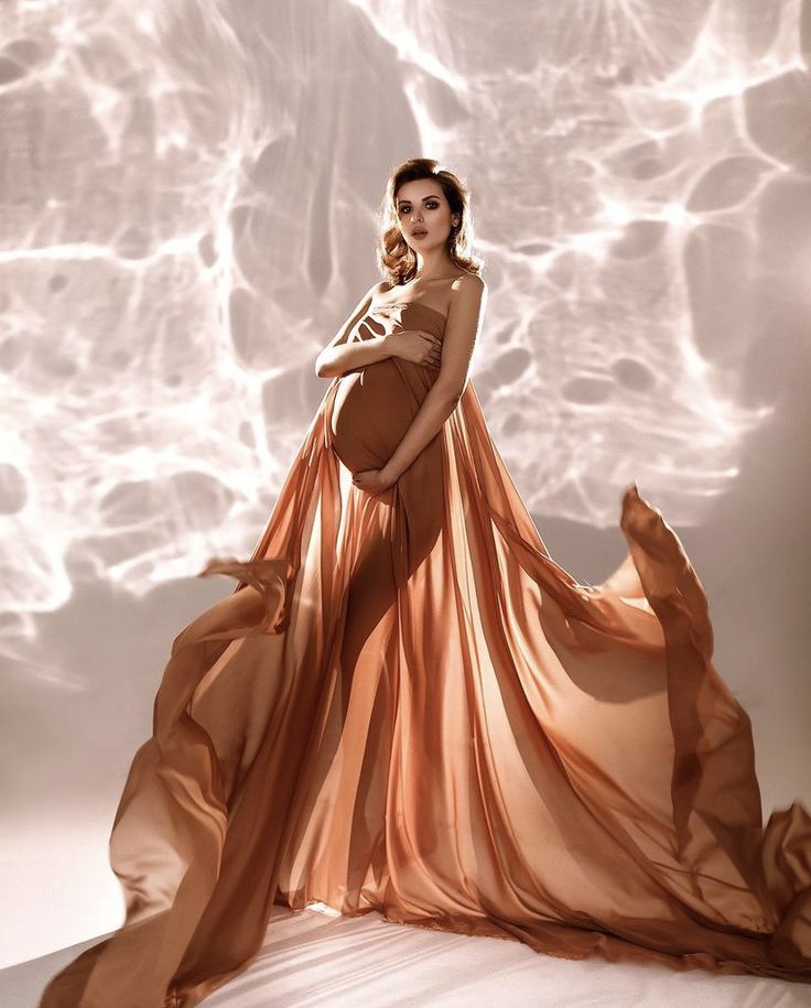 a pregnant woman in a flowing dress poses for a photo shoot with her belly exposed