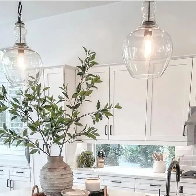 a kitchen with white cabinets and an island in the middle is lit by two hanging lights