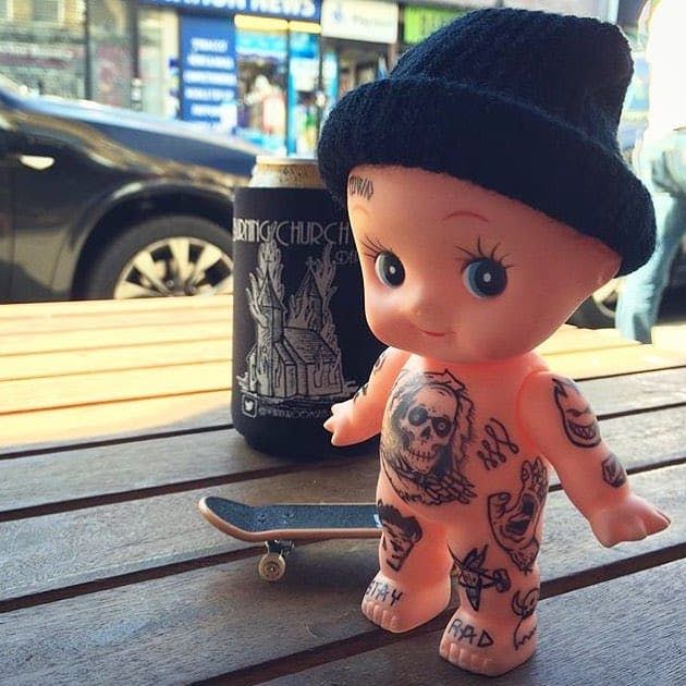 a small toy doll sitting on top of a wooden table next to a skateboard