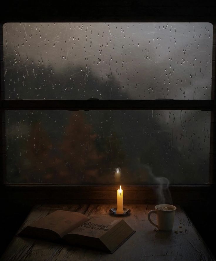 a candle is lit next to an open book on a table with a cup of coffee