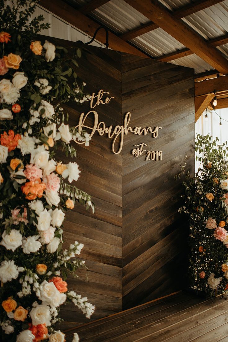 a wooden wall with flowers and greenery on it that says the dougahans