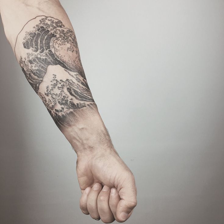 a man's arm with a wave tattoo on it and his hand in the air