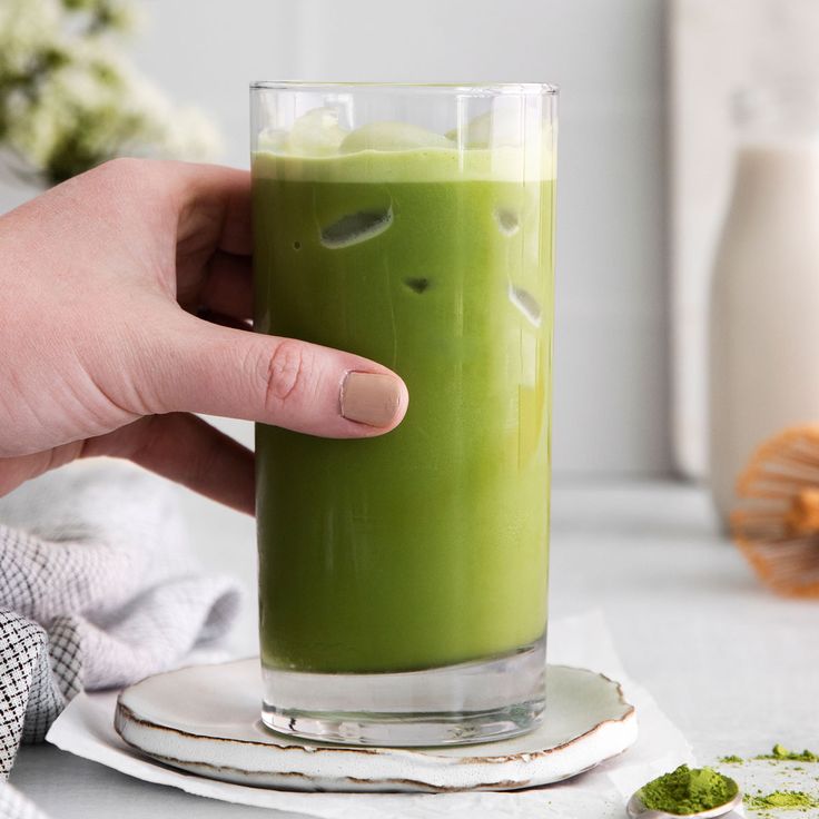 a person holding a glass with green liquid in it