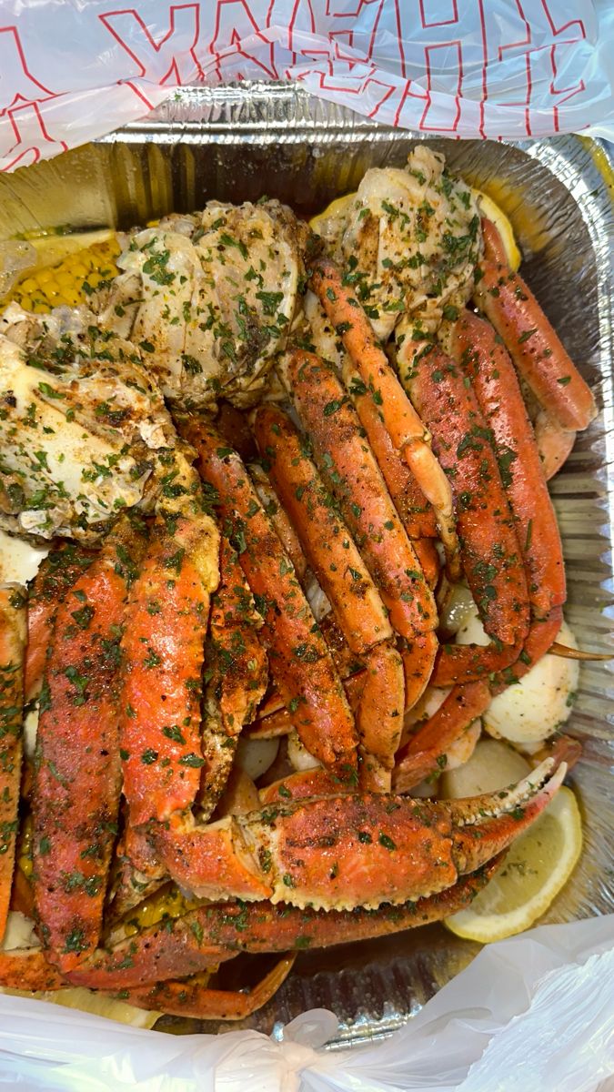 cooked crab legs with lemon wedges and parsley on top in a foil container