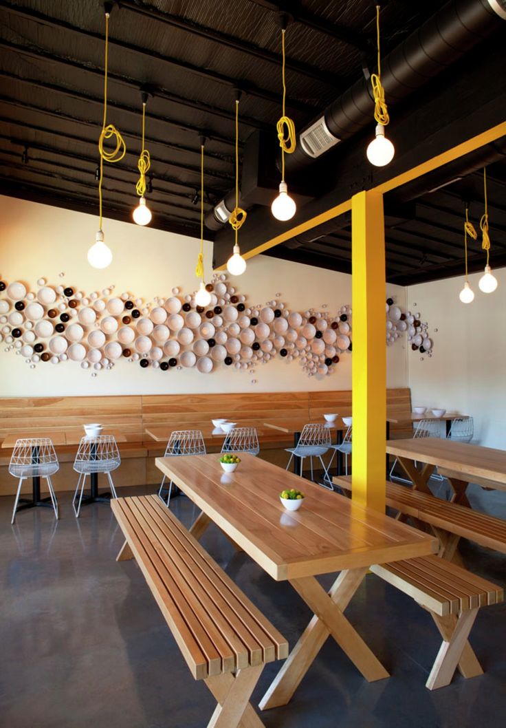 a wooden table and benches in a room with lights hanging from the ceiling above it