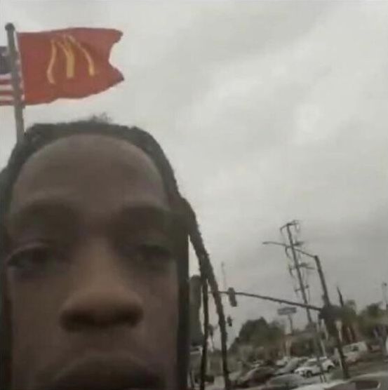 a man with dreadlocks standing in front of a mcdonald's sign and a red flag